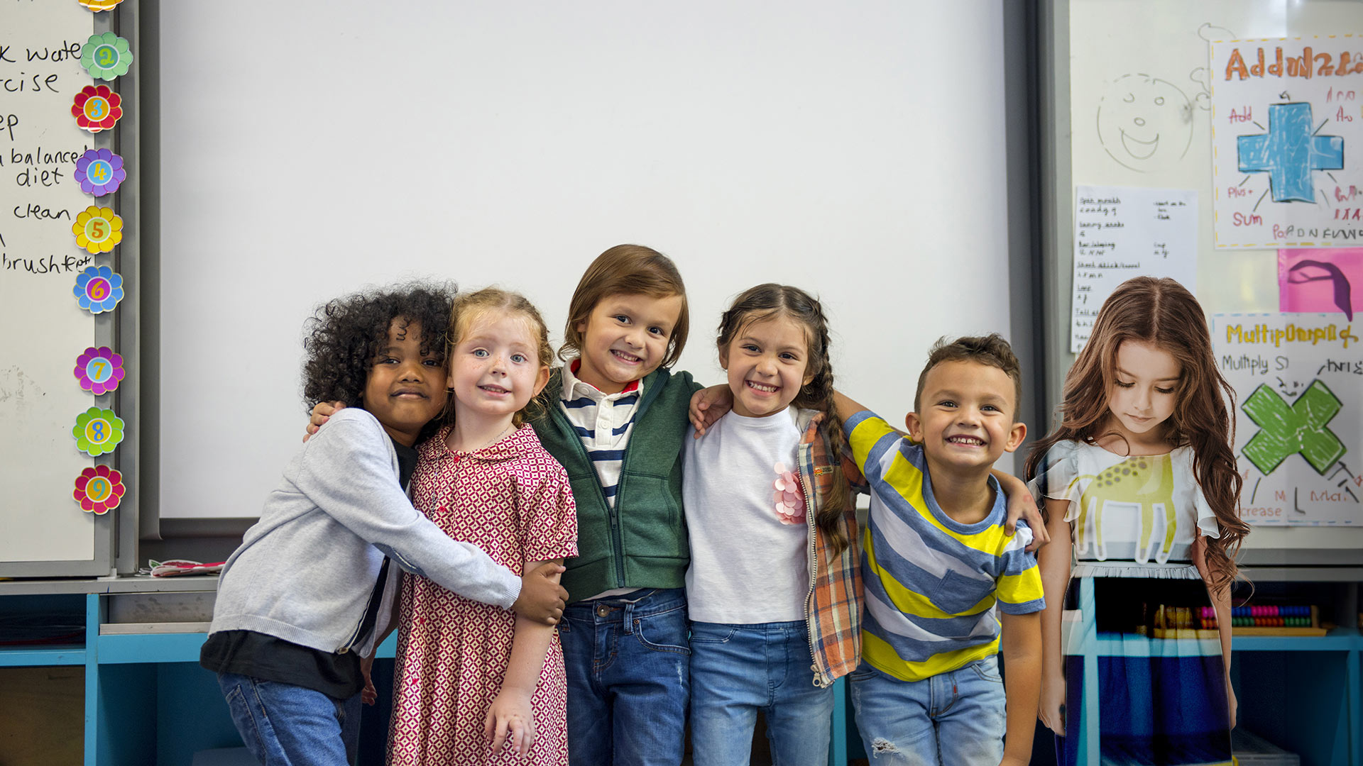 Photo of kids smiling and hugging in front of a white board